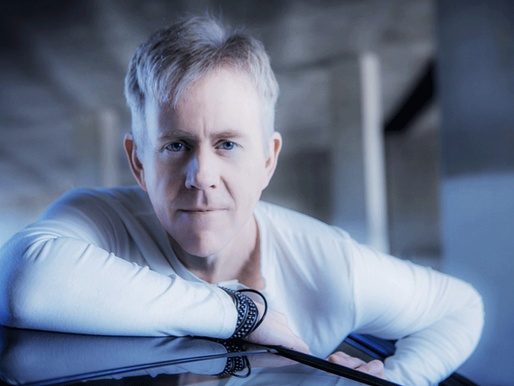 Serious gray-haired man in a white shirt leans on a car in a cool blue garage, staring at the camera.
