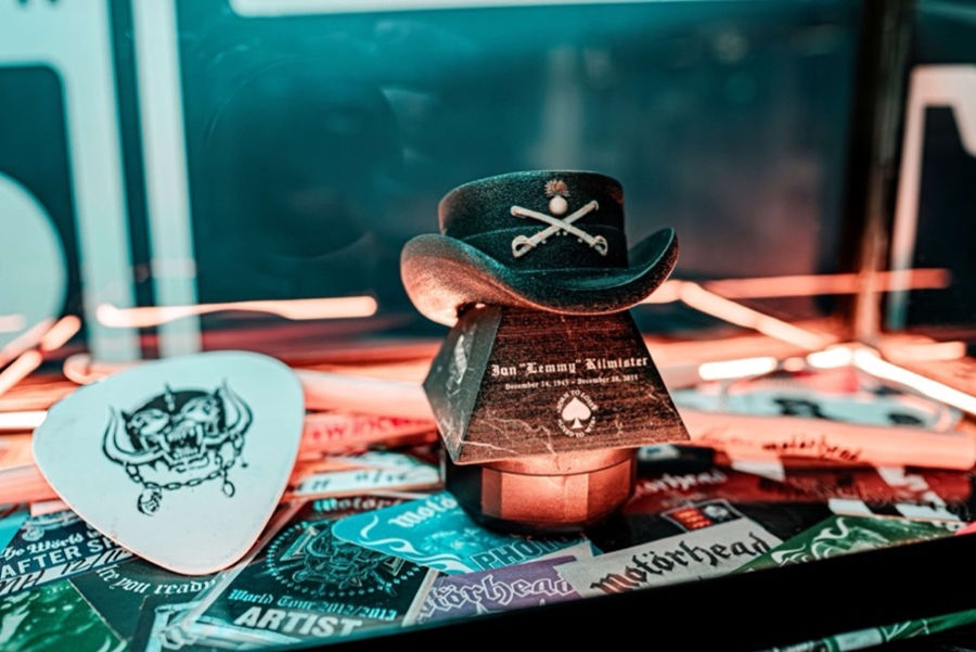 Small black cowboy hat with skull emblem on colorful guitar picks in a neon-lit display case, with partial label text visible
