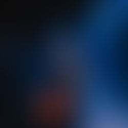 Musician on stage plays guitar and sings into mic, right arm raised. Blue spotlighting, dim background, and emotional, energetic mood.