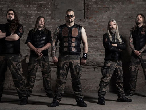 Five men in camo pants and black vests stand confidently against a brick wall, exuding a strong, determined mood.