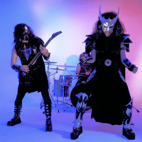 Band in metallic costumes playing instruments on stage with colorful lighting; intense and energetic mood.