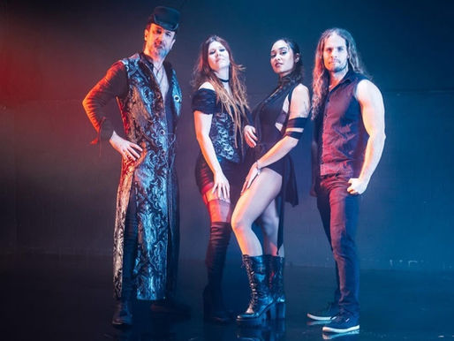 Four people in stylish black and silver outfits pose confidently under blue and red lighting in a dark studio setting.