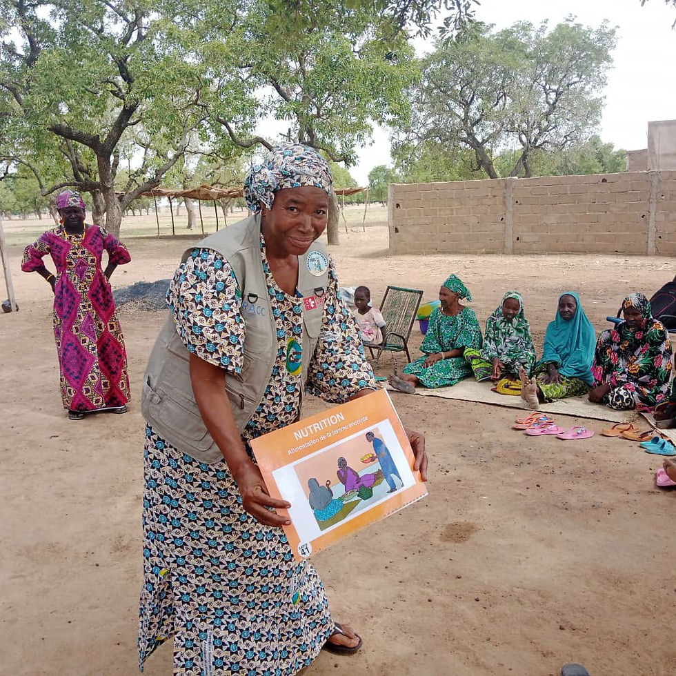 Femme souriante tenant un livret Nutrition lors d’une séance communautaire en plein air, femmes assises sous les arbres.