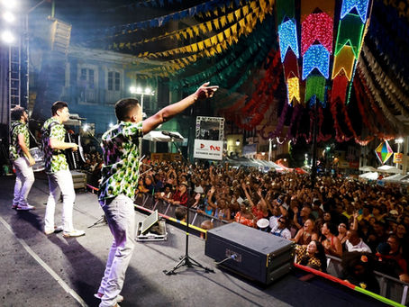 Banda em palco de festa junina canta para multidão animada, sob bandeirolas coloridas e luzes neon à noite