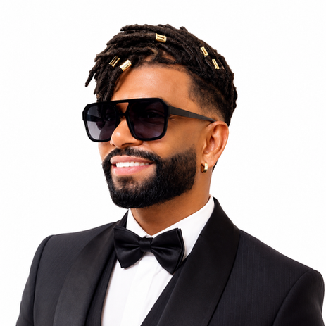 Cantor Silvanno Salles está sorridente de smoking preto e óculos escuros, com dreadlocks e detalhes dourados, em fundo branco.