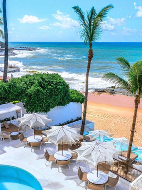 Área externa do Principote com piscina, mesas, coqueiros e vista para o mar no Rio Vermelho, em Salvador.