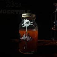 A mason jar half-filled with a red liquid. A tall bird-like sticker labels the jar on the front.
