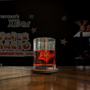 An orange cocktail in a low glass hold a sphere of ice encasing a piece of star fruit.