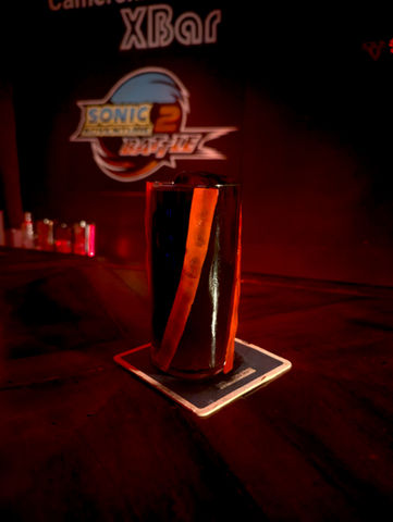 A jet black drink in a tall glass with red pepper skin highlights twisting around the sides of the glass. The blackboard behind the drink sports the logo of Sonic Adventure 2: Battle.