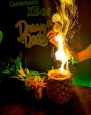 A pillar of sparks and flames curl above a pineapple with a missing head and a straw sticking out of it. The severed head lies to the side.