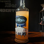 A glass bottle filled with a pink liquid. The bottle is labeled 'Endogeny' and has a sticker of a 6-legged dog monster with a wide mouth.