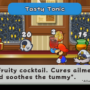 The shop in the Excess Express has a counter lined with products including a Mystery Box, a Boo's Sheet, Tasty Tonic, Maple syrup, and a Super Shroom. Mario and Bobbery stand in front of the realistic Tasty Tonic and inspect it. The top of the screen titles "Tasty Tonic" and the bottom describes "A fruity cocktail. Cures ailments and soothes the tummy*. *Allegedly"