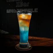 A layered drink in a tall conical glass. The layers form a gradient easing from a light brown to a light blue from the top to the bottom.