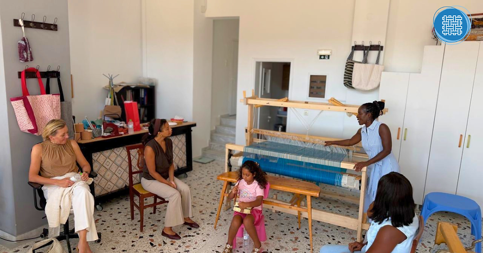 Women and a child gather in a bright weaving studio as one woman demonstrates a loom, with bags and supplies on the walls.