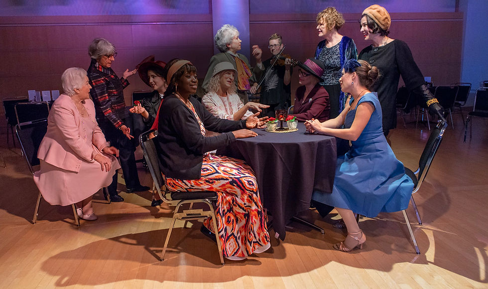 several actors sitting and standing near a table