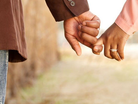 A couple holding hands outdoors, with an engagement ring and a softly blurred, warm-toned background