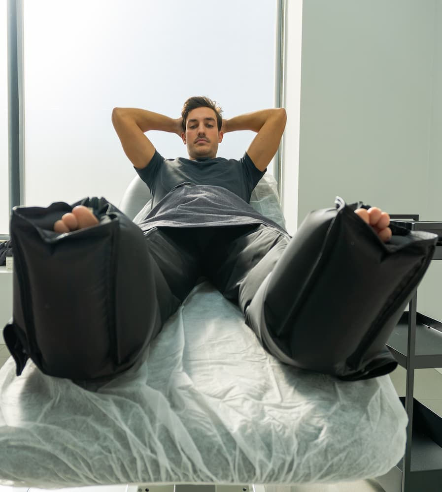 Man relaxing on a medical table with compression boots in a bright room. He has his arms behind his head and looks comfortable. normatec compression at oasis cryo in san antonio texas
