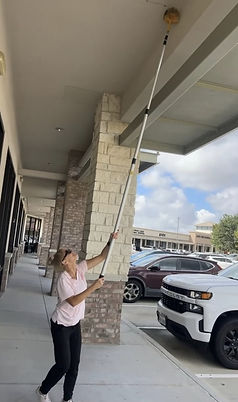 Alco Pest Control technician removing cobwebs from a commercial shopping center in Spring, TX.