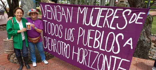 Two women holding a book together next to a big feminist purple banner