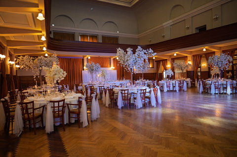 Svadobná výzdoba vo Veľkej Dvorane v Ružomberku bola ukážkou toho, ako môže aj veľká sála pôsobiť elegantne, luxusne a harmonicky. Dominantným prvkom sa stali naše kvetinové a čerešňové stromy, ktoré pôsobili majestátne, no zároveň jemne dopĺňali atmosféru priestoru.
Celkový vzhľad sme podčiarkli čírymi a zlatými dekoráciami, doplnili sme živé kvety a postarali sa o decentné osvetlenie, ktoré vytvorilo čarovnú svadobnú atmosféru. Kombinácia výškových dekorácií, detailne prepracovaných prvkov a kvalitných materiálov premenila sálu na priestor, ktorý pôsobil sviežo, nadčasovo a premyslene.
Naše kvetinové a čerešňové stromy sú ideálnym riešením pre veľké sály, kde dodajú luxus a vzdušnosť. Sú vhodné ako výzdoba hlavného stola, doplnok ku kruhovým stolom hostí alebo ako výrazná dominanta v priestore.
Ak plánujete svadbu vo väčšej sále, aj tá môže pôsobiť exkluzívne. Radi pre vás pripravíme návrh svadobnej výzdoby na mieru – od Ružomberka, cez Námestovo a Dolný Kubín až po celý Žilinský kraj.