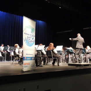 A concert band performing on stage under the festival banner