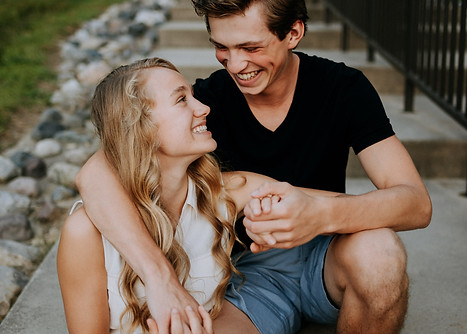 young couple sitting on the sidewalk hugging and smiling at each other