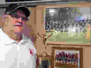 A long-time football and lacrosse coach at Kenwood and Edgewood, Fred Myers, the 1968 Unsung Hero winner, shows off his trophy and watch while standing next to a photo of his 1995 Kenwood team. No. 55 in that photo is Earl Henson, who also won the top prize at the Unsung Hero banquet.