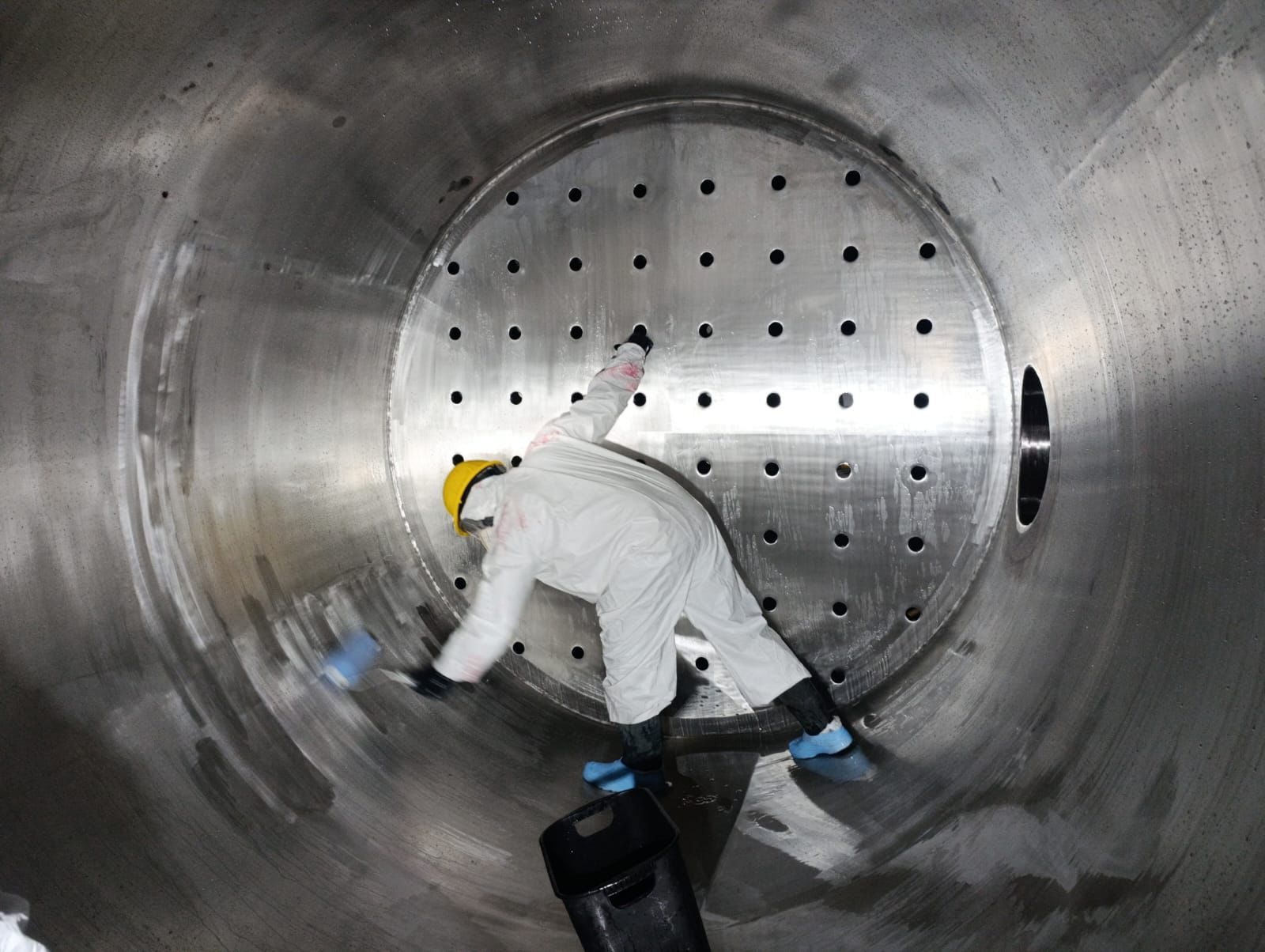 Técnico con traje de protección limpiando el interior de un tanque de acero inoxidable