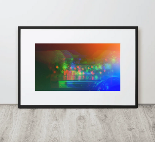 View from a car's interior at night through a rain-streaked windshield, showing the dashboard and blurred blue and orange str