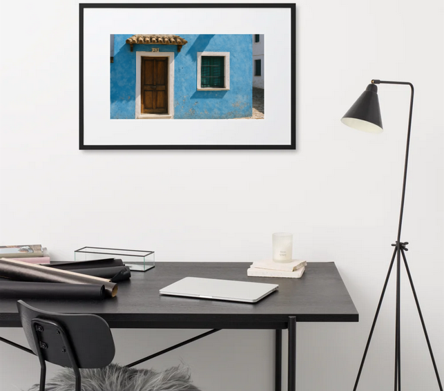 A small two-story Spanish-style house painted bright blue, with a terracotta tile roof, white window frames