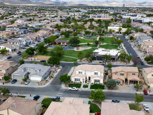 Aerial view of a modern Las Vegas suburban neighborhood with rows of single‑family homes, clean streets, and a central community park with green space, playground, and gazebo, set against distant mountains.