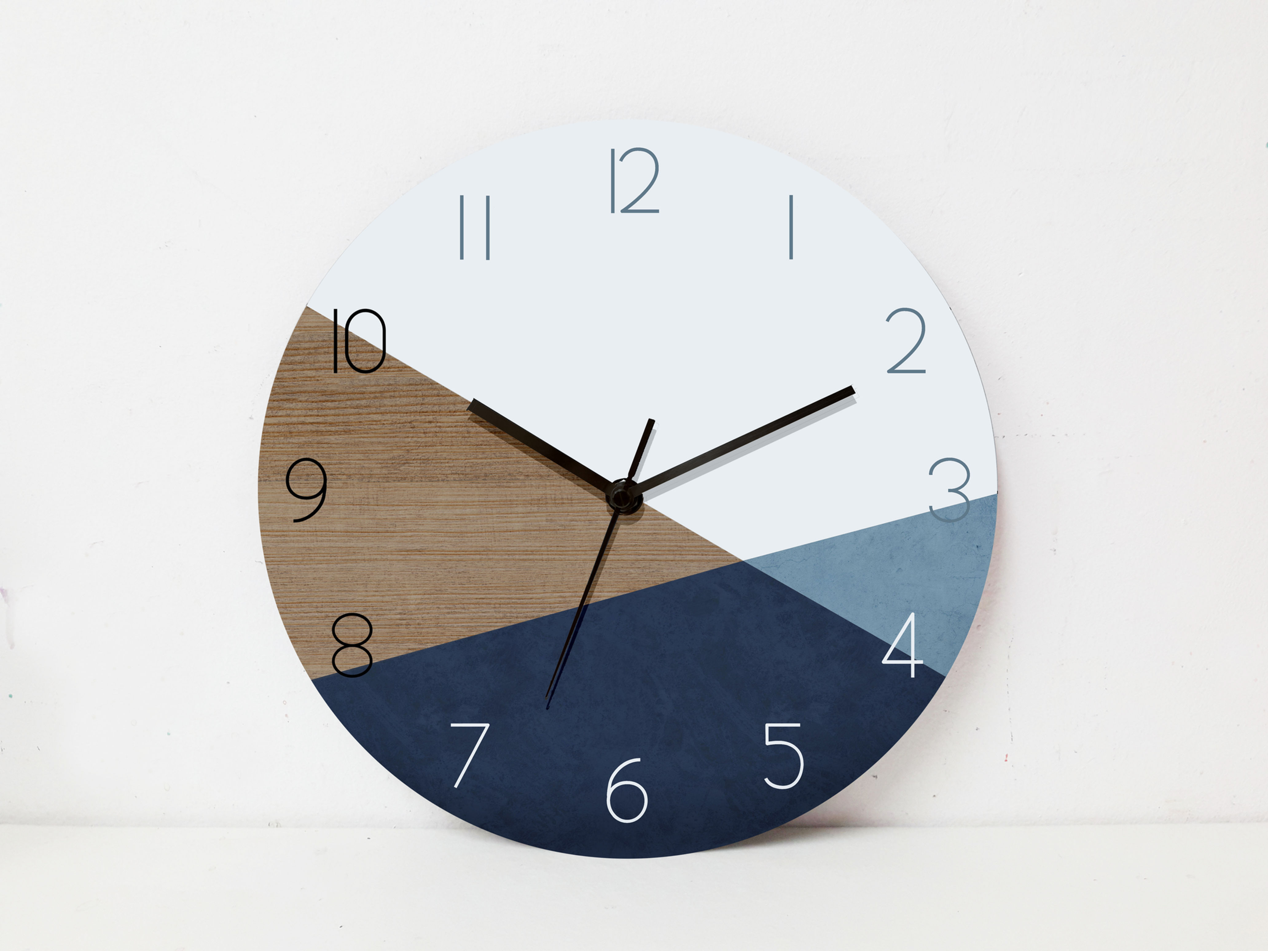 שעון עגול עם חלוקה צבעונית בעץ, כחול כהה וכחול בהיר. הספרות 1–12 מודפסות בלבן על רקע גיאומטרי.