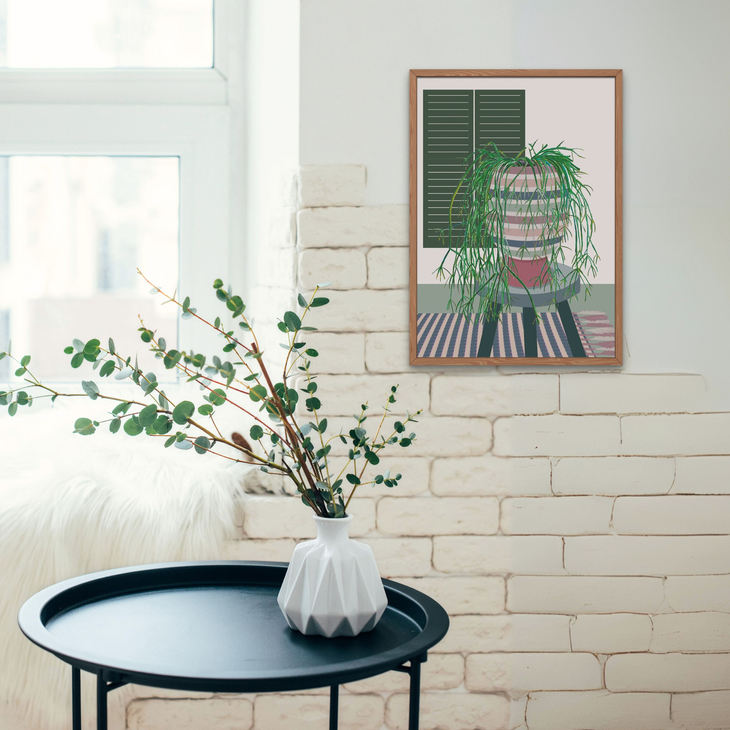 ציור ממוסגר תלוי על קיר לבנים לבן, לצד שולחן שחור עם אגרטל מודרני וענפי צמח ירוק.