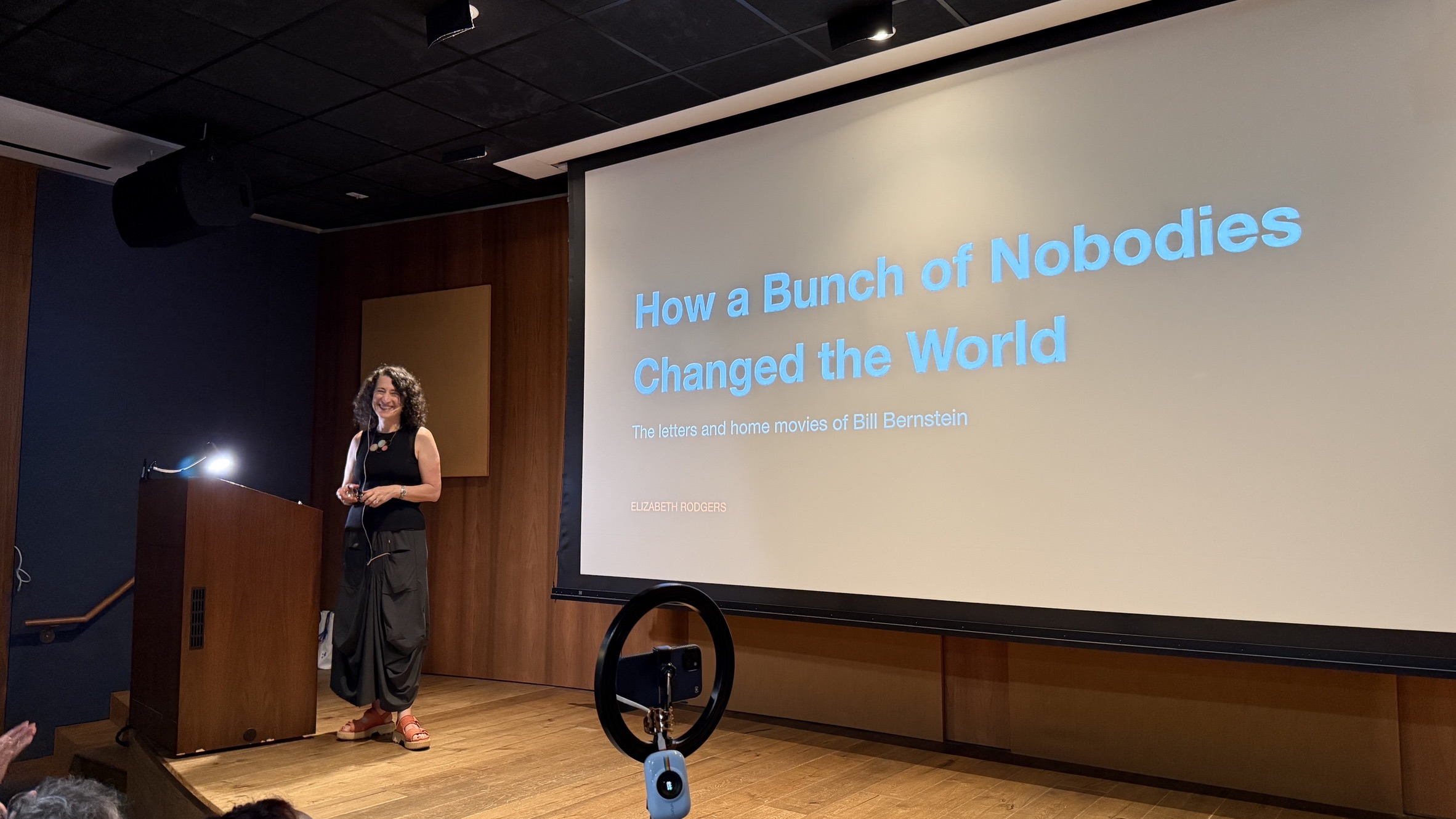 Elizabeth Rodgers smiling on stage beside a large screen showing the talk title
