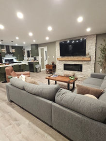 Finished open-concept living room with fireplace and kitchen in background in renovated cottage.