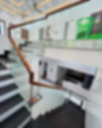 Modern interior with black and white staircase, glass railing, and ceiling fans. Green baskets on the upper level. Bright, minimalist design.