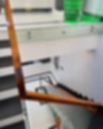 A staircase with wooden railings and glass panels, leading to a white floor. Green laundry baskets are on the upper landing.
