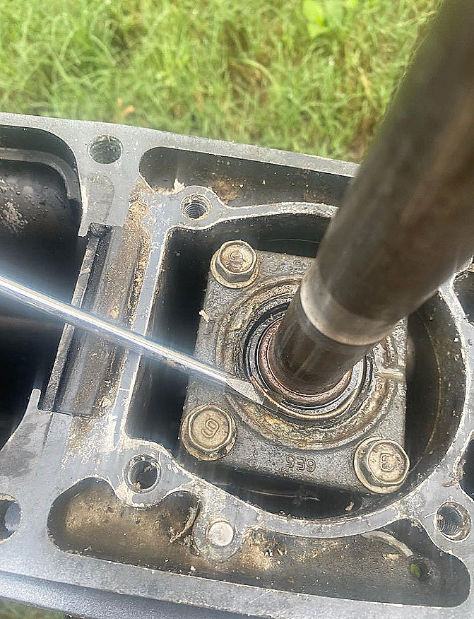 Close-up of a metal driveshaft being worked on inside a dirty outboard lower unit housing with a screwdriver.