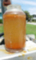 Clear jar of fuel contaminated with water on a metal surface outdoors, with blurred grass and sky in the background.