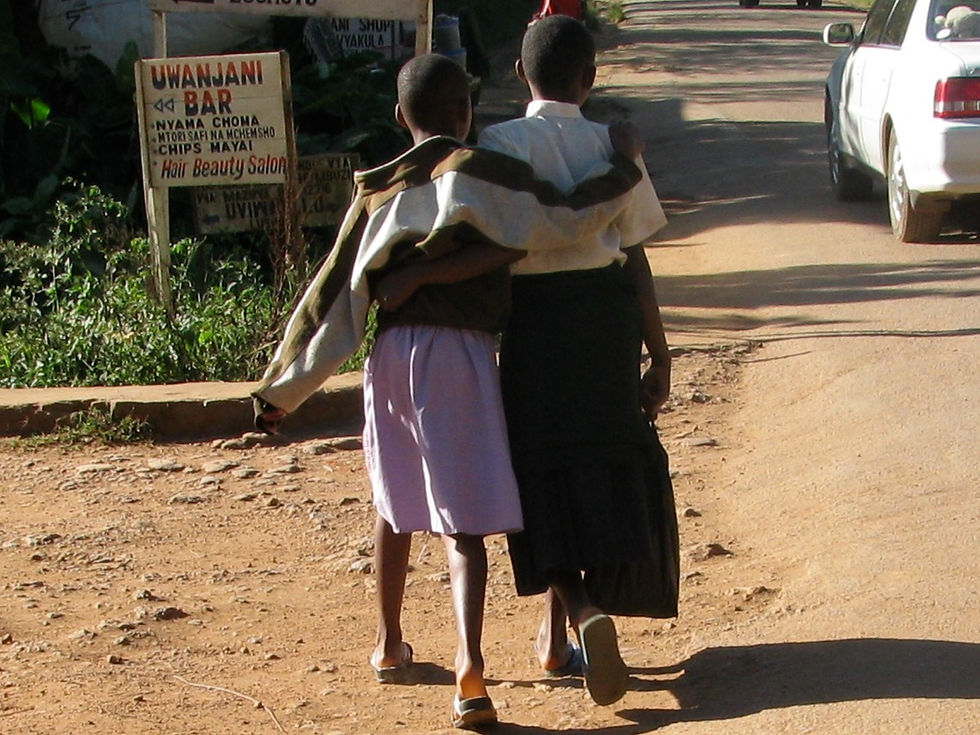 Two girls with arms around each other walk down a dusty street in Lushoto, Tanzania.