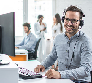 Servicemitarbeiter mit Headset am PC in Großraumbüro