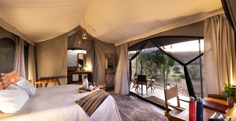 Guest safari tent wtih double bed and dressing table to an open sided tent leading to the deck at Basecamp Wilderness Camp in Naboisho, Masai Mara, Kenya