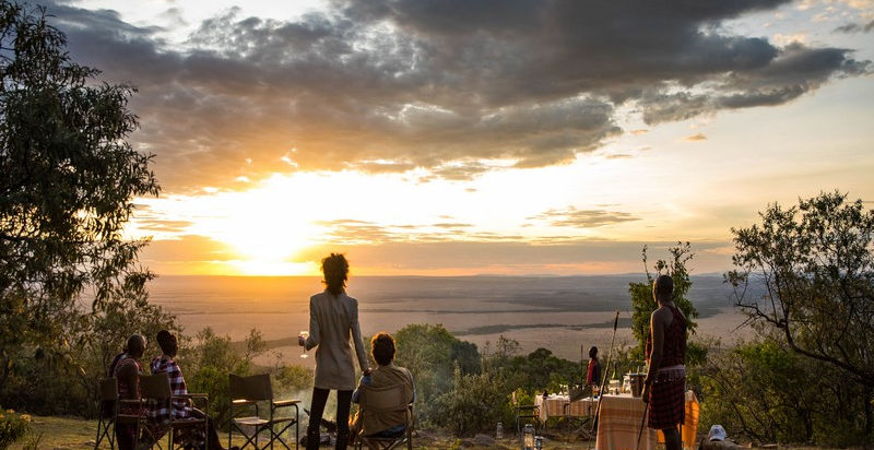 Couple enjoying the view across the Masai Mara and having a drink served by a traditional Maasai warrior at Saruni Wild Camp in The Greater Masai Mara, Kenya