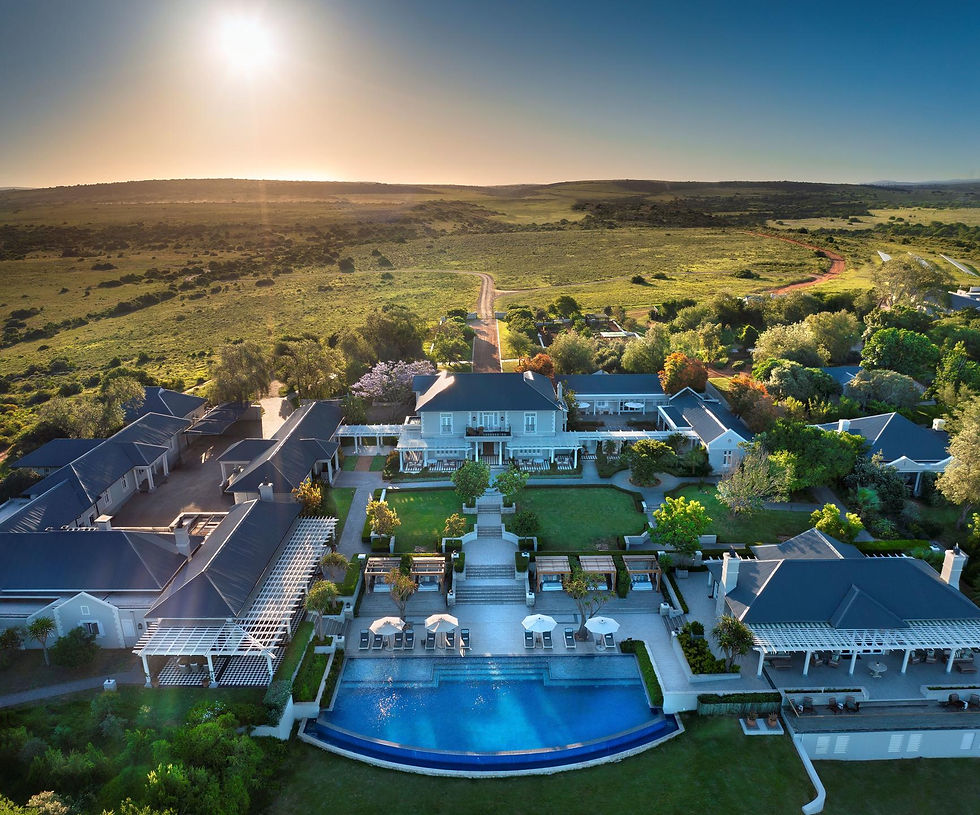 Aerial view of a stunning safari lodge with a swimming pool and multiple buildings surrounded by lush green grass overlooking the plains of Shamwari Private Game Reserve in South Africa