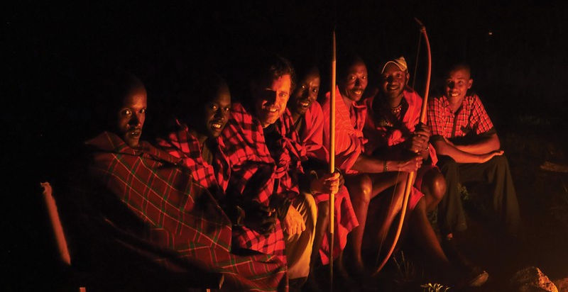 Group of 7 Maasai warriors by the camp fire at night time at Basecamp Wilderness Camp in Naboisho, Masai Mara, Kenya