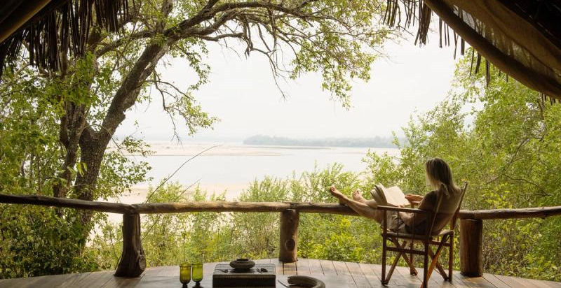Lady reading a book on the deck overlooking the river at Sands River Safari Camp in Nyerere in Tanzania with Safari Ambitions