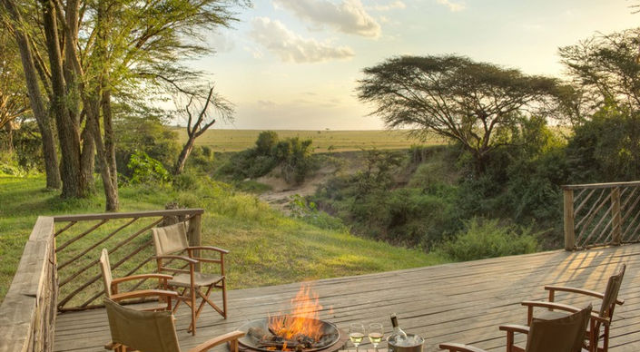4 safari chairs on the deck in front of a camp fire overlooking the plains and trees at Basecamp Masai Mara Camp by the Talek River in The Masai Mara in Kenya
