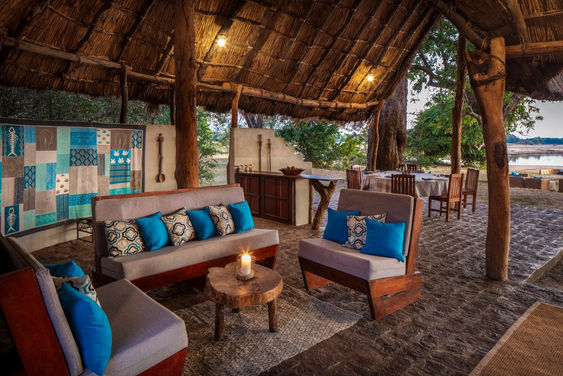 2 sofas and armchairs with blue cushions in an open sided thatched cottage at Takwela Camp