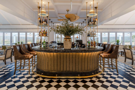 Circular bar with high chairs, hanging lights and plants sitting on a black and white tiled floor