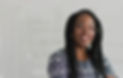 A smiling Black woman with long box braids and a nose ring standing next to a whiteboard with diagram sketches